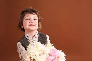 Photo of Cute little boy with bouquet of beautiful peonies on brown background. Space for text