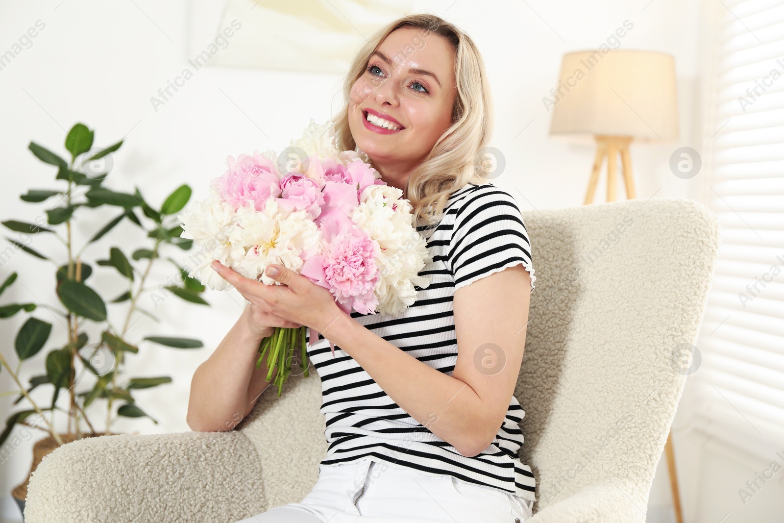 Photo of Happy woman with bouquet of beautiful peonies in armchair indoors