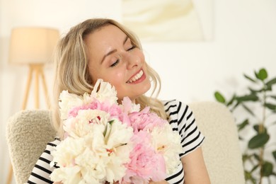 Photo of Happy woman with bouquet of beautiful peonies in armchair indoors