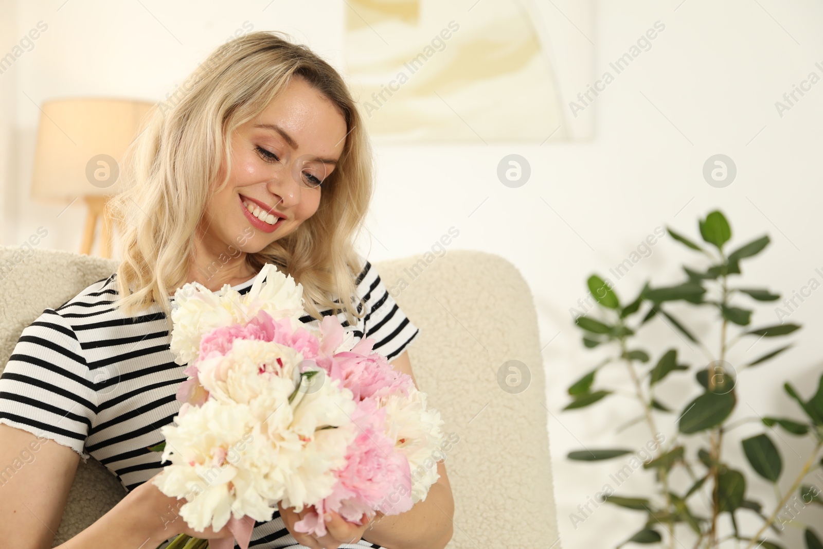 Photo of Happy woman with bouquet of beautiful peonies in armchair indoors, space for text