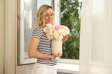 Photo of Happy woman with bouquet of beautiful peonies near window indoors