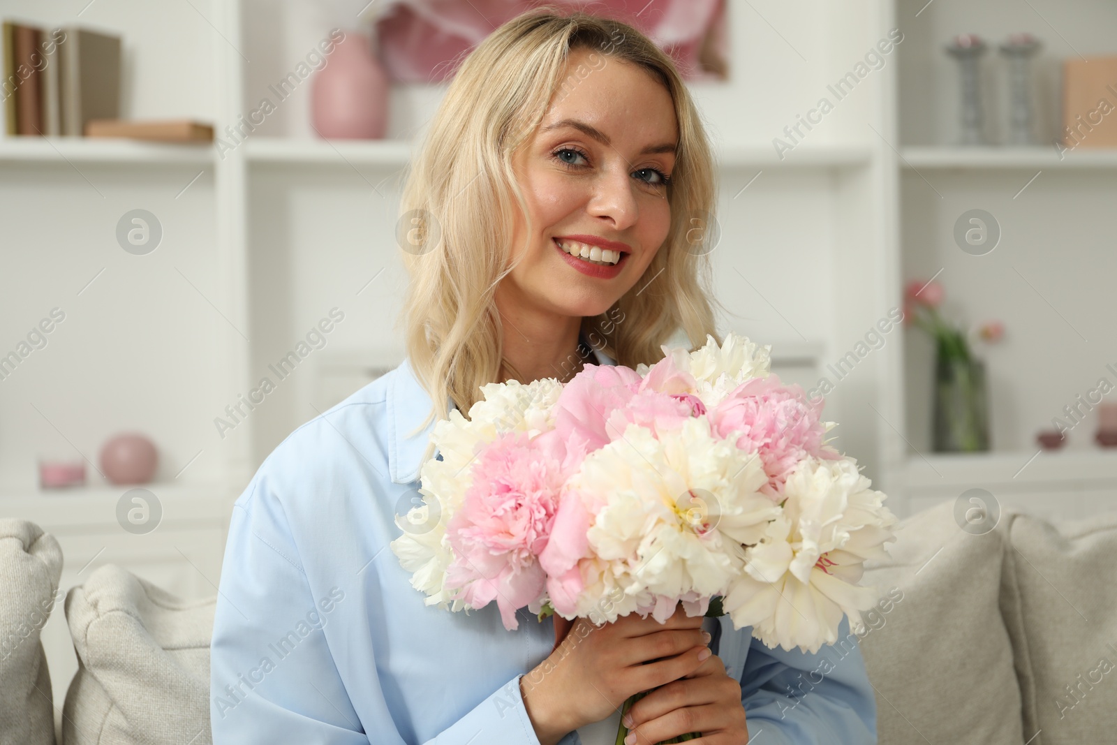 Photo of Happy woman with bouquet of beautiful peonies on sofa at home