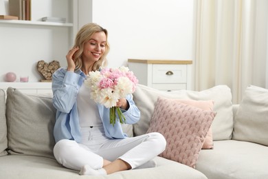 Photo of Happy woman with bouquet of beautiful peonies on sofa at home
