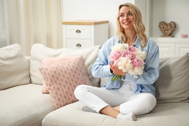 Photo of Happy woman with bouquet of beautiful peonies on sofa at home
