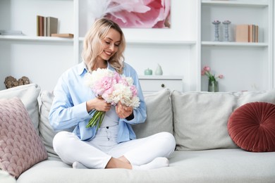 Photo of Happy woman with bouquet of beautiful peonies on sofa at home
