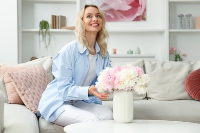 Photo of Happy woman with bouquet of beautiful peonies at home