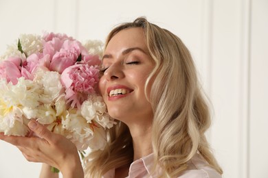 Photo of Happy woman with bouquet of beautiful peonies near white wall indoors
