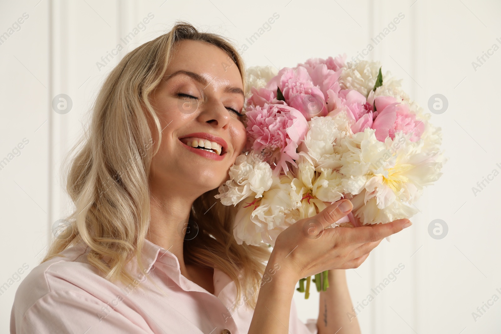 Photo of Happy woman with bouquet of beautiful peonies near white wall indoors