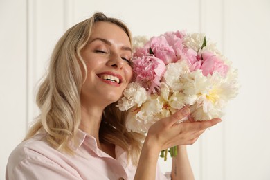 Photo of Happy woman with bouquet of beautiful peonies near white wall indoors