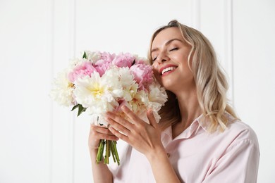 Photo of Happy woman with bouquet of beautiful peonies near white wall indoors