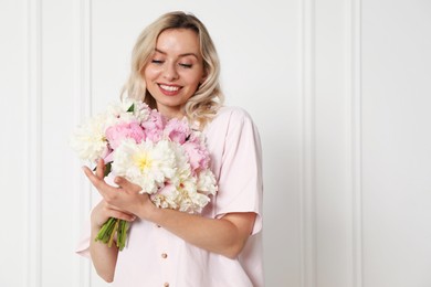 Photo of Happy woman with bouquet of beautiful peonies near white wall indoors, space for text
