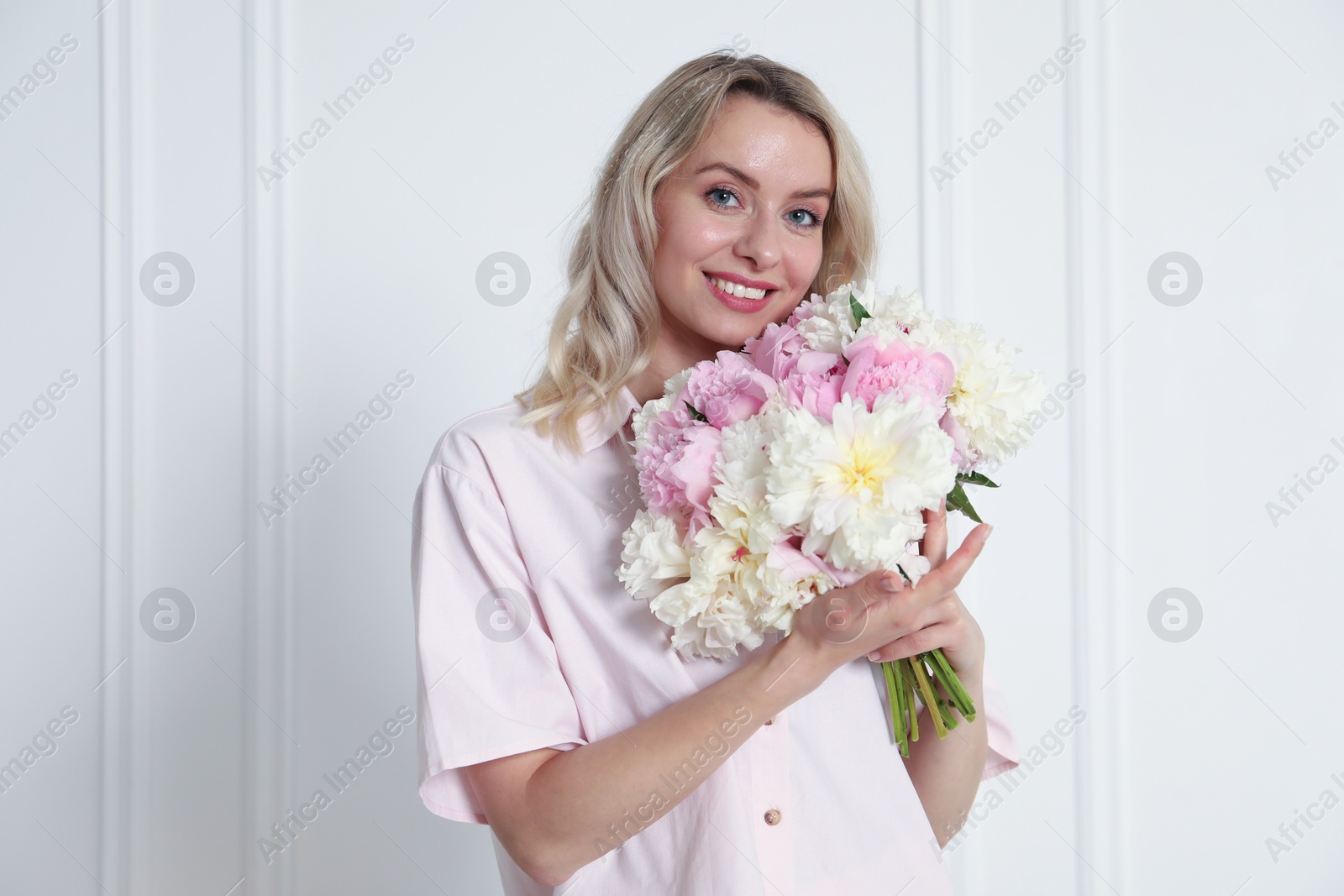 Photo of Happy woman with bouquet of beautiful peonies near white wall indoors