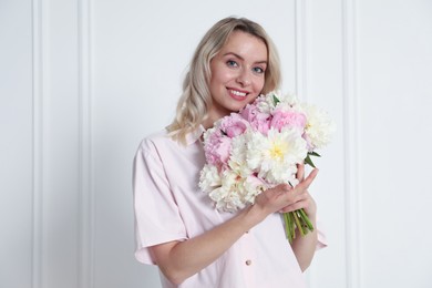 Photo of Happy woman with bouquet of beautiful peonies near white wall indoors