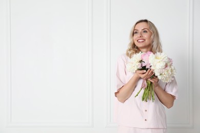 Photo of Happy woman with bouquet of beautiful peonies near white wall indoors, space for text