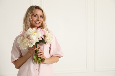 Photo of Happy woman with bouquet of beautiful peonies near white wall indoors, space for text