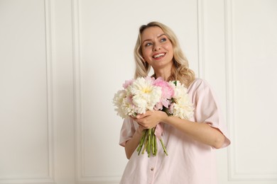 Photo of Happy woman with bouquet of beautiful peonies near white wall indoors, space for text
