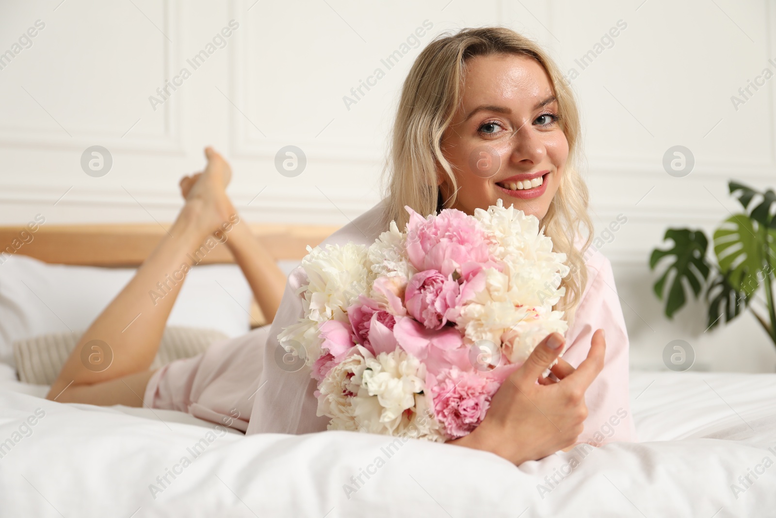 Photo of Happy woman with bouquet of beautiful peonies on bed indoors