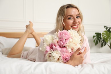 Photo of Happy woman with bouquet of beautiful peonies on bed indoors