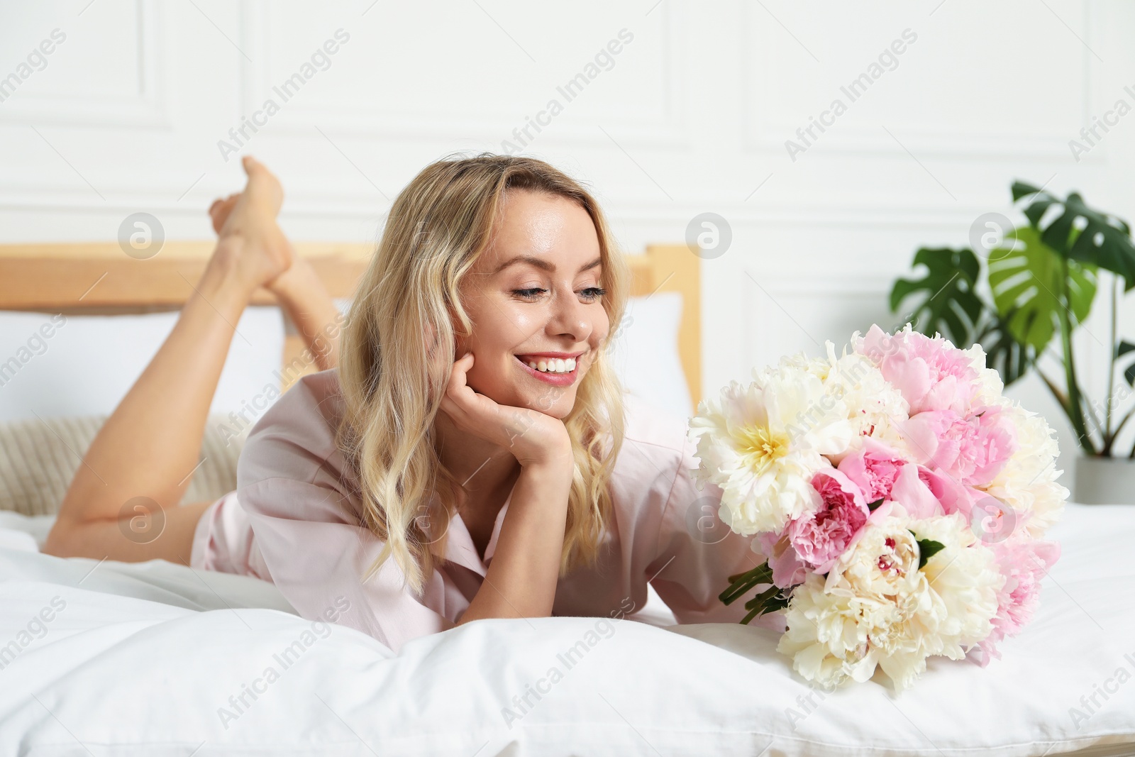 Photo of Happy woman with bouquet of beautiful peonies on bed indoors
