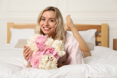 Photo of Happy woman with bouquet of beautiful peonies on bed indoors