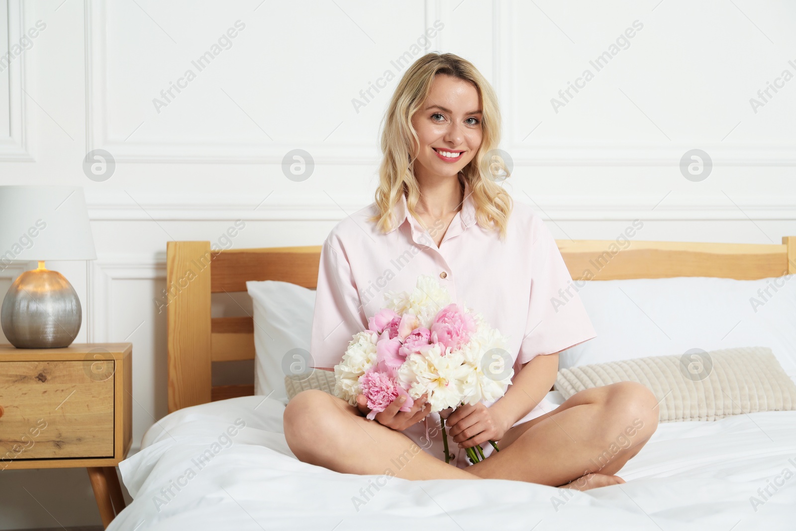 Photo of Happy woman with bouquet of beautiful peonies on bed indoors