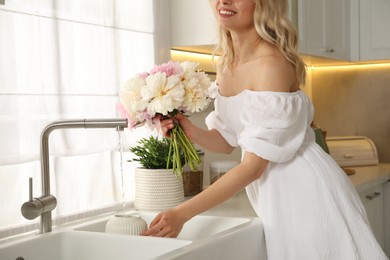 Photo of Woman taking care of beautiful peonies in kitchen, closeup