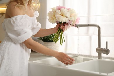 Photo of Woman taking care of beautiful peonies in kitchen, closeup