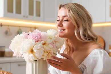 Photo of Happy woman with bouquet of beautiful peonies in kitchen