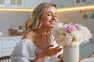 Photo of Happy woman with bouquet of beautiful peonies in kitchen