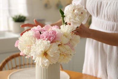 Photo of Woman making bouquet of beautiful peonies at table in kitchen, closeup