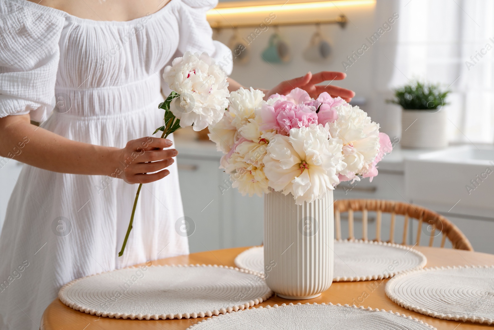 Woman making bouquet of beautiful peonies at table in kitchen, closeup Photo of Woman making bouquet of beautiful peonies at table in kitchen, closeup