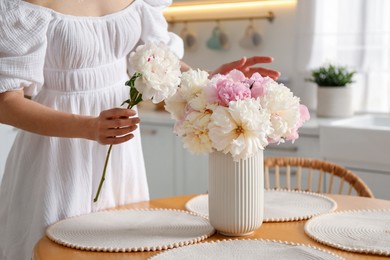 Photo of Woman making bouquet of beautiful peonies at table in kitchen, closeup