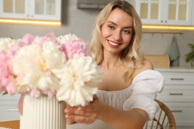 Photo of Happy woman with bouquet of beautiful peonies in kitchen