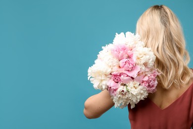 Photo of Woman with bouquet of beautiful peonies on light blue background, back view. Space for text