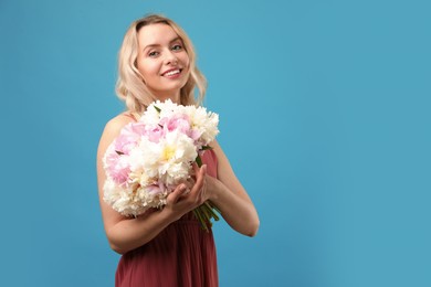 Photo of Happy woman with bouquet of beautiful peonies on light blue background, space for text