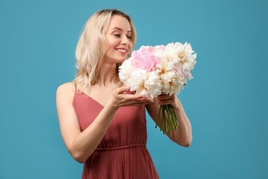 Photo of Happy woman with bouquet of beautiful peonies on light blue background