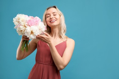 Photo of Happy woman with bouquet of beautiful peonies on light blue background, space for text