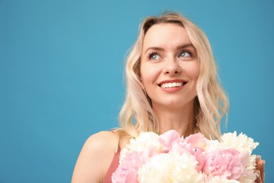 Photo of Happy woman with bouquet of beautiful peonies on light blue background