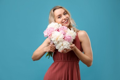 Photo of Happy woman with bouquet of beautiful peonies on light blue background
