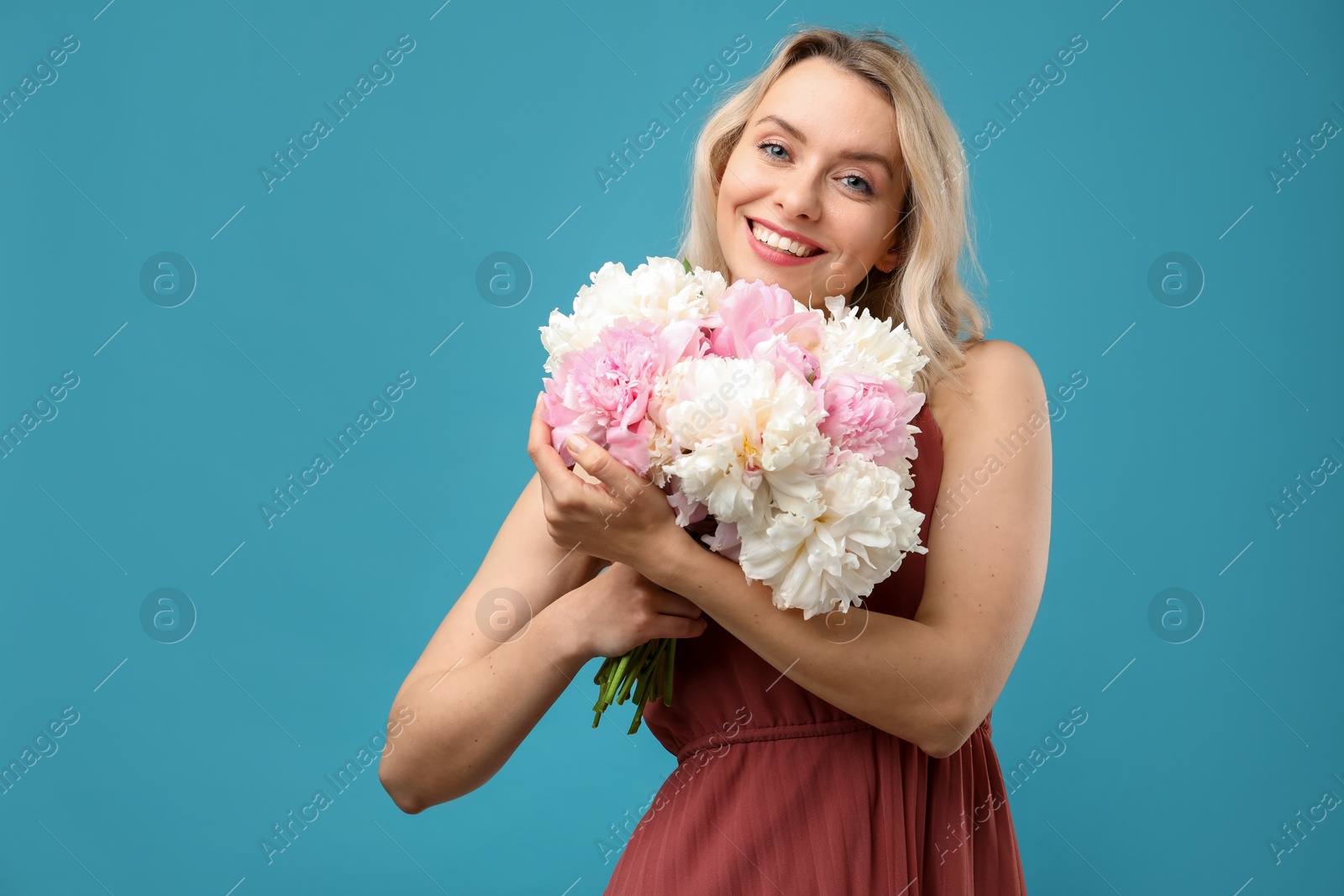 Photo of Happy woman with bouquet of beautiful peonies on light blue background