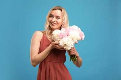 Photo of Happy woman with bouquet of beautiful peonies on light blue background