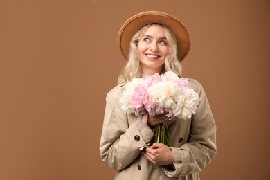 Photo of Happy woman with bouquet of beautiful peonies on brown background, space for text