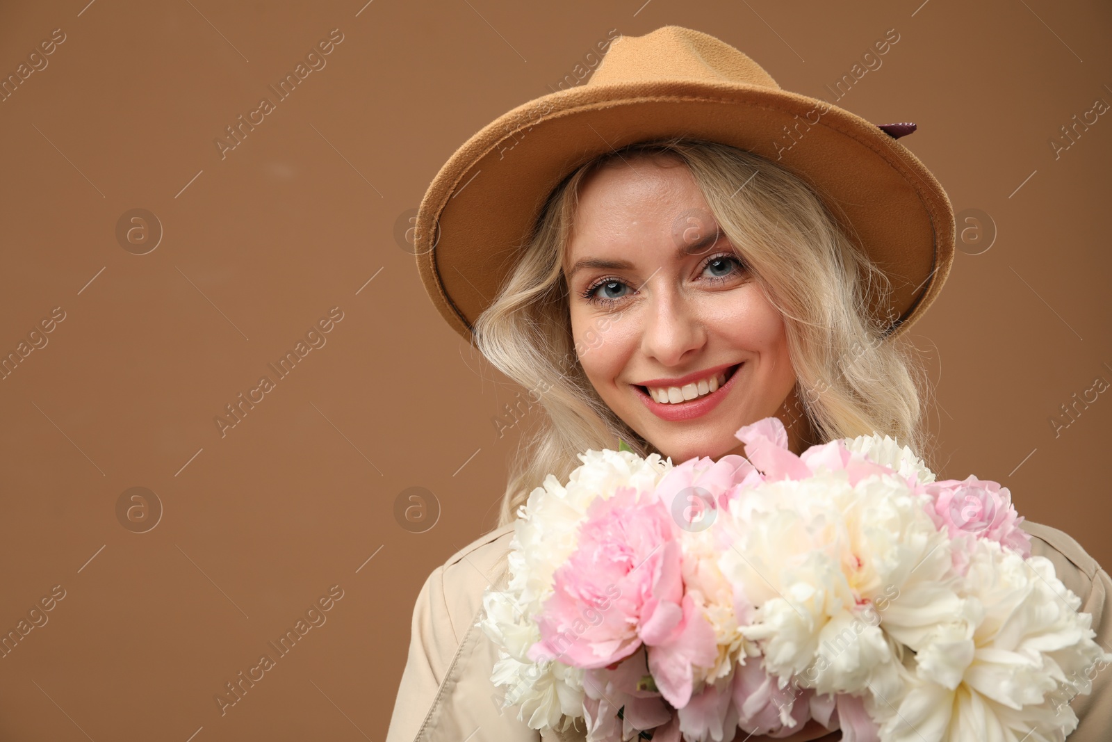 Photo of Happy woman with bouquet of beautiful peonies on brown background, space for text