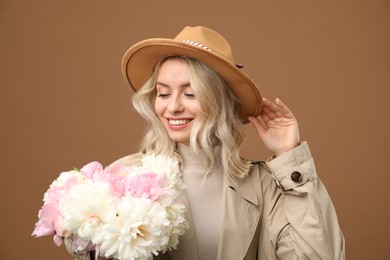 Photo of Happy woman with bouquet of beautiful peonies on brown background