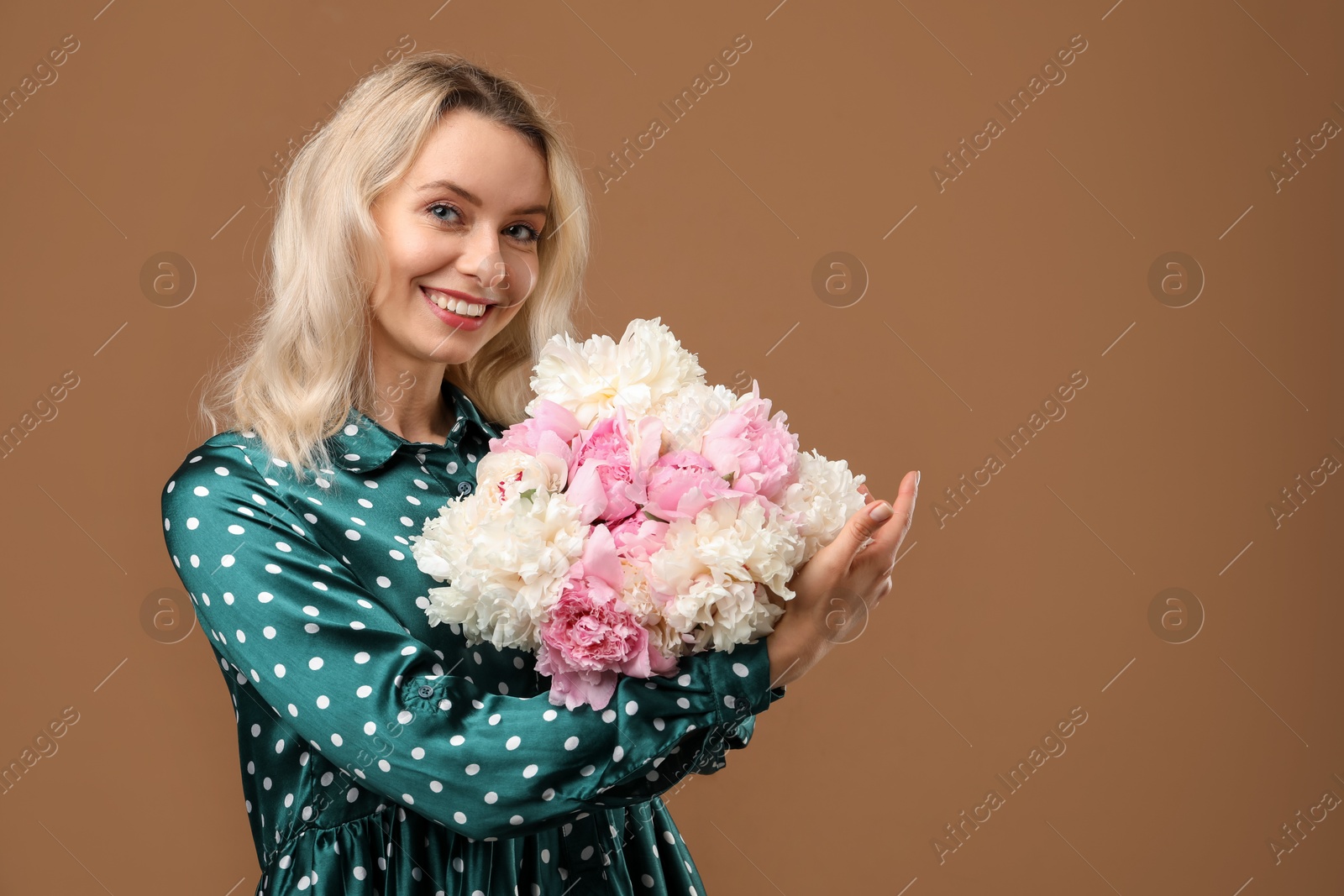 Photo of Happy woman with bouquet of beautiful peonies on brown background, space for text
