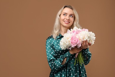 Photo of Happy woman with bouquet of beautiful peonies on brown background, space for text