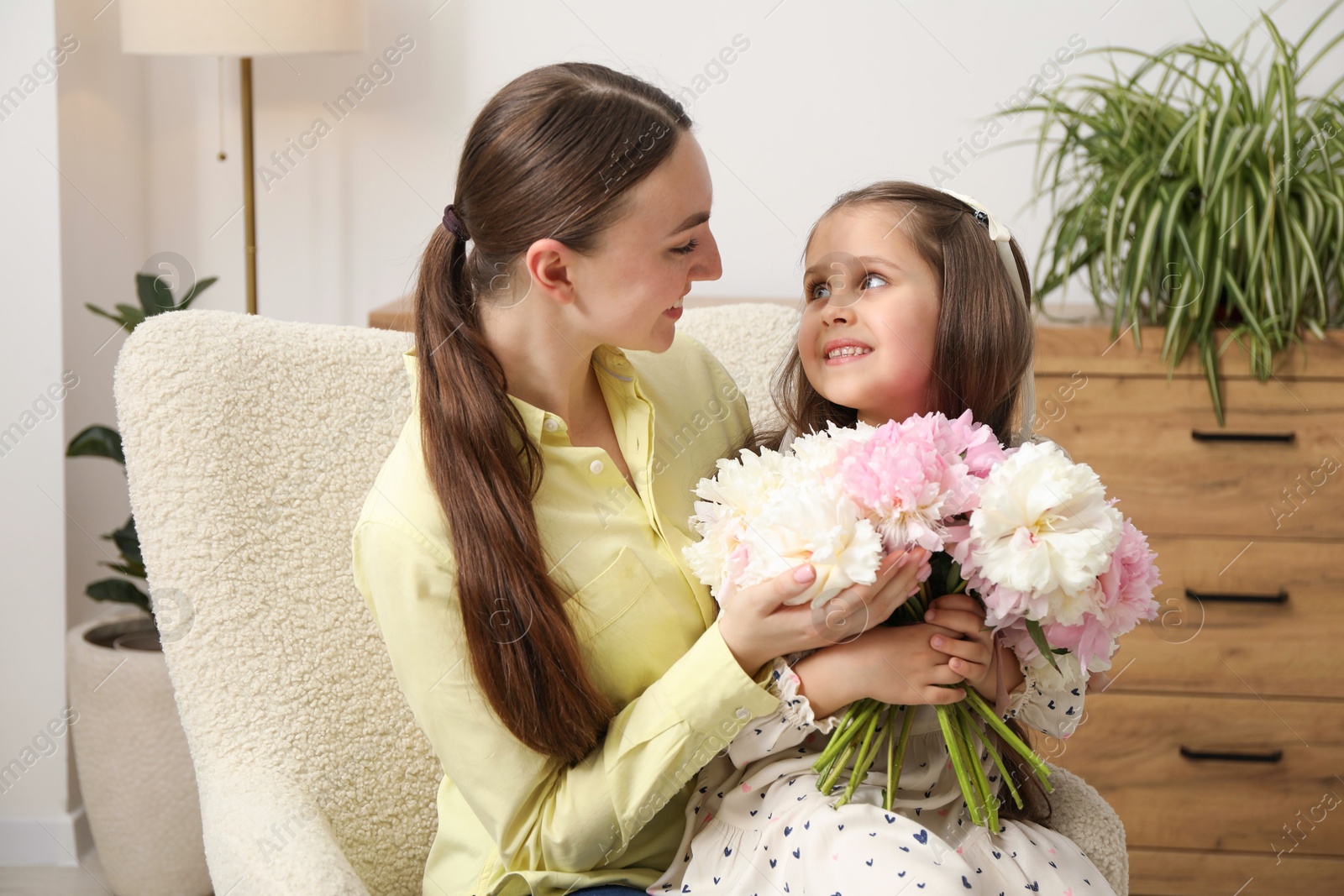 Photo of Cute little girl giving her mother bouquet of beautiful peonies at home