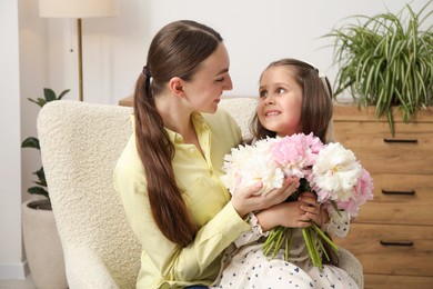 Photo of Cute little girl giving her mother bouquet of beautiful peonies at home