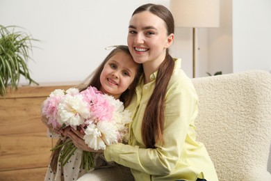 Photo of Cute little girl giving her mother bouquet of beautiful peonies at home