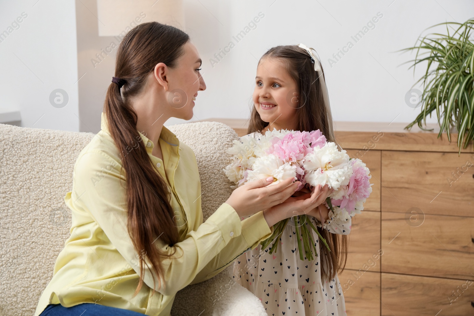 Photo of Cute little girl giving her mother bouquet of beautiful peonies at home